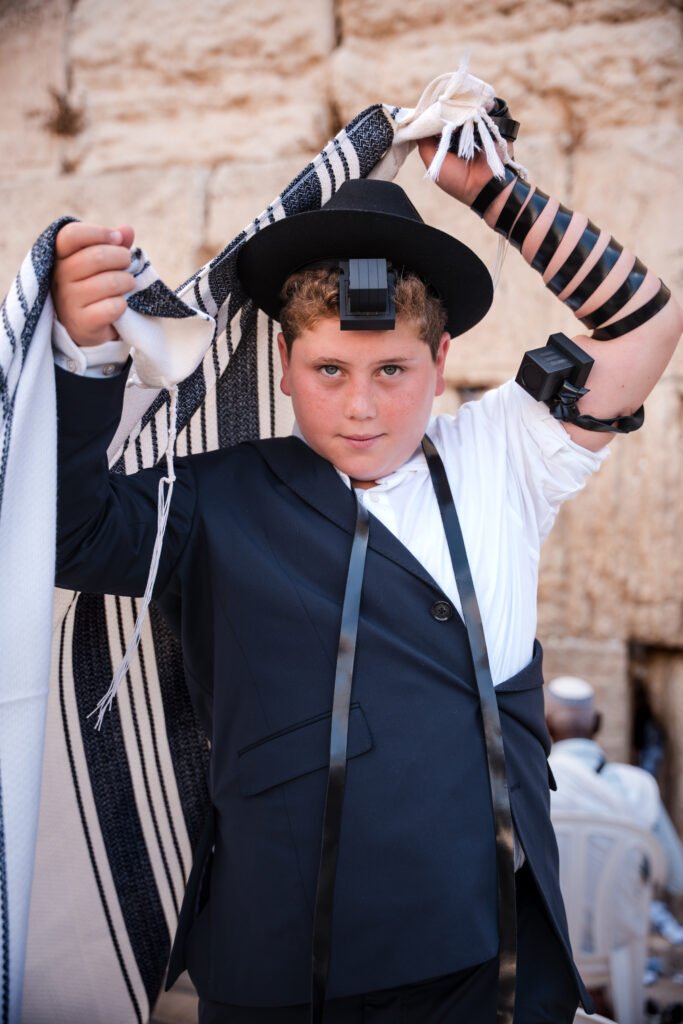 Young Jewish boy wearing a tallit (prayer shawl) and tefillin (phylacteries) for his Bar Mitzvah ceremony.