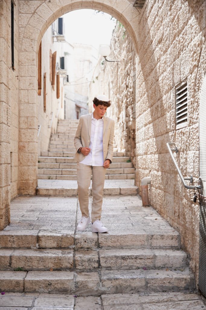 Boy wearing a beige suit, white shirt, and kippah walking down stone steps under an archway in Jerusalem’s Old City