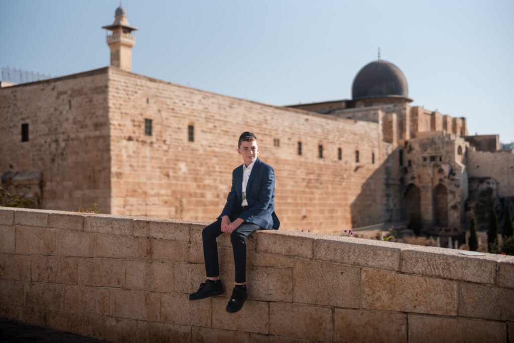 Bar Mitzvah boy sitting on the wall with the Western Wall in the background, Jerusalem.