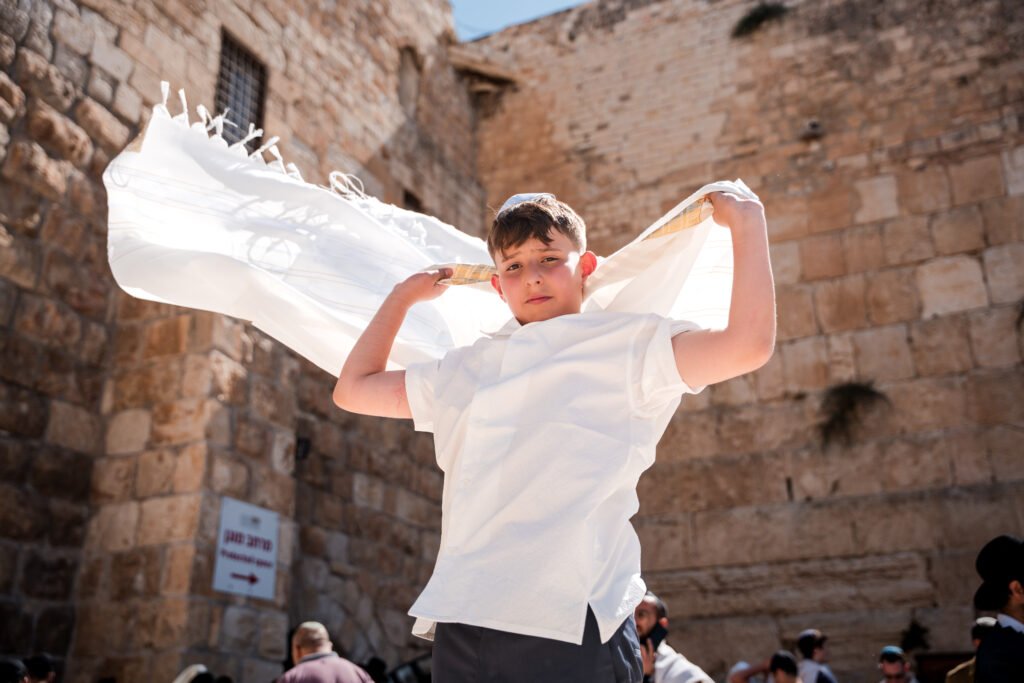 Boy lifting a tallit beside the stone walls of Jerusalem