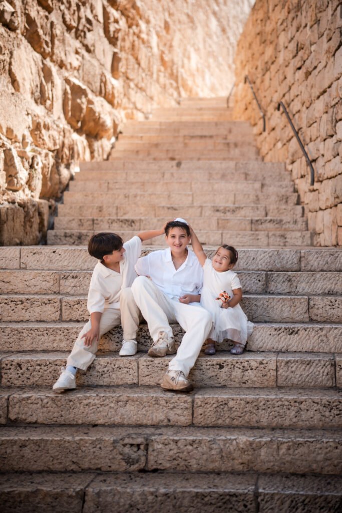 Brother and sister placing their hands on their Bar Mitzvah brother’s head on the steps in Jerusalem’s Old City.