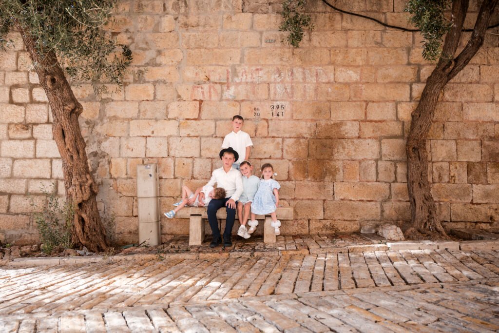 Children sitting together beneath trees beside an Old City stone wall
