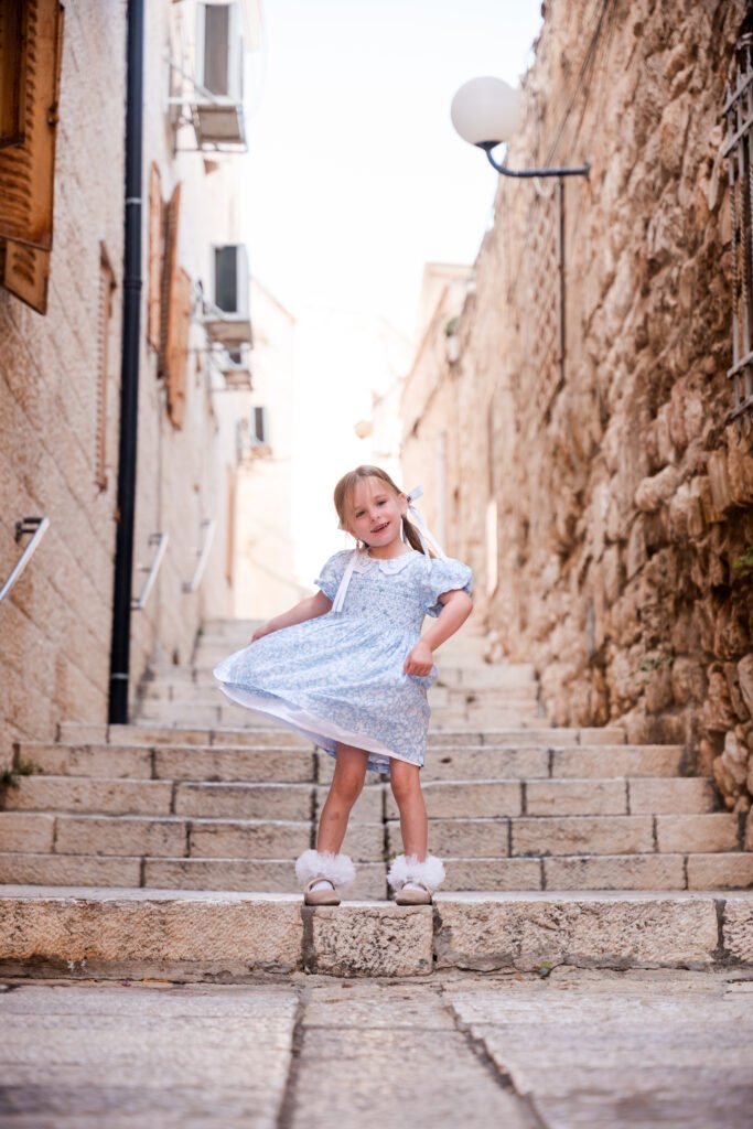 Girl looking at the camera while playing with her dress on HaMalakh Street in Jerusalem’s Old City.