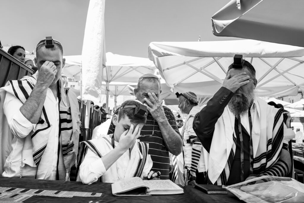 Black and white photograph of three people wearing tefillin during prayer