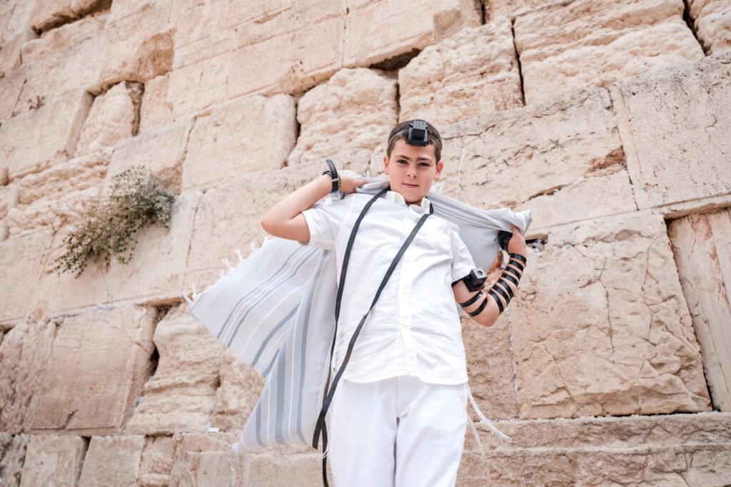 Boy wearing tefillin and holding a tallit beside the Kotel stones