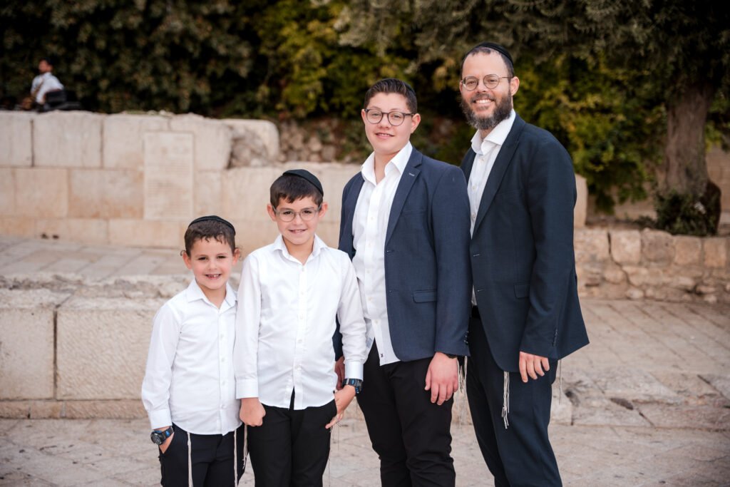 Group portrait of a man and three boys beside a Jerusalem stone wall