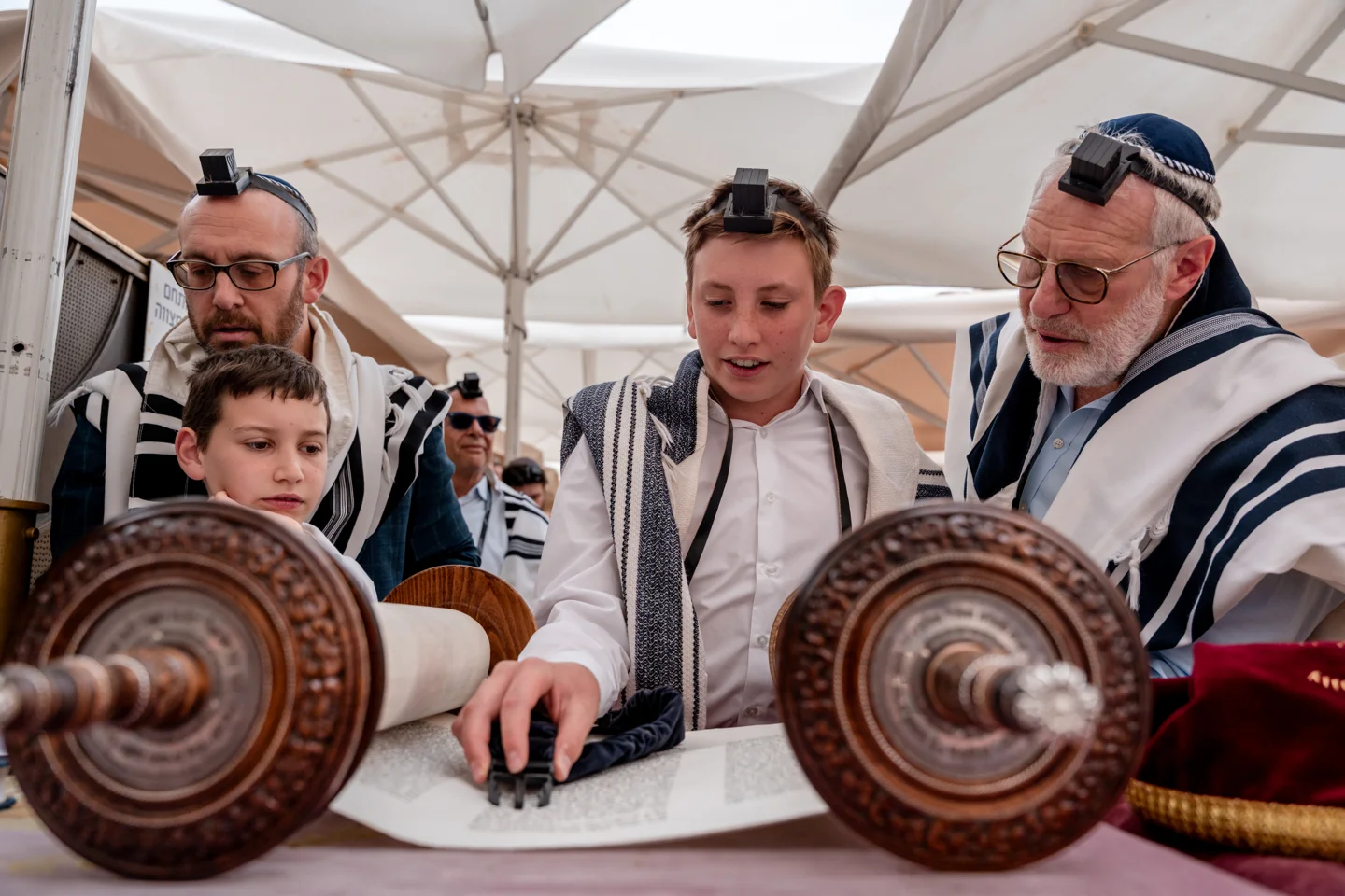 A Bar Mitzvah boy reading from the Torah with his family at the Kotel