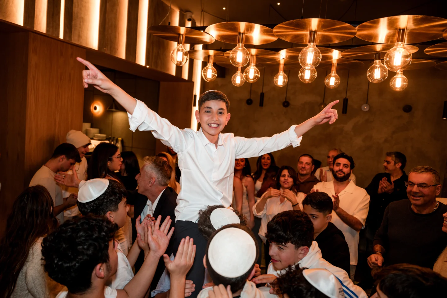 A Bar Mitzvah boy celebrating on a guest’s shoulders in a restaurant